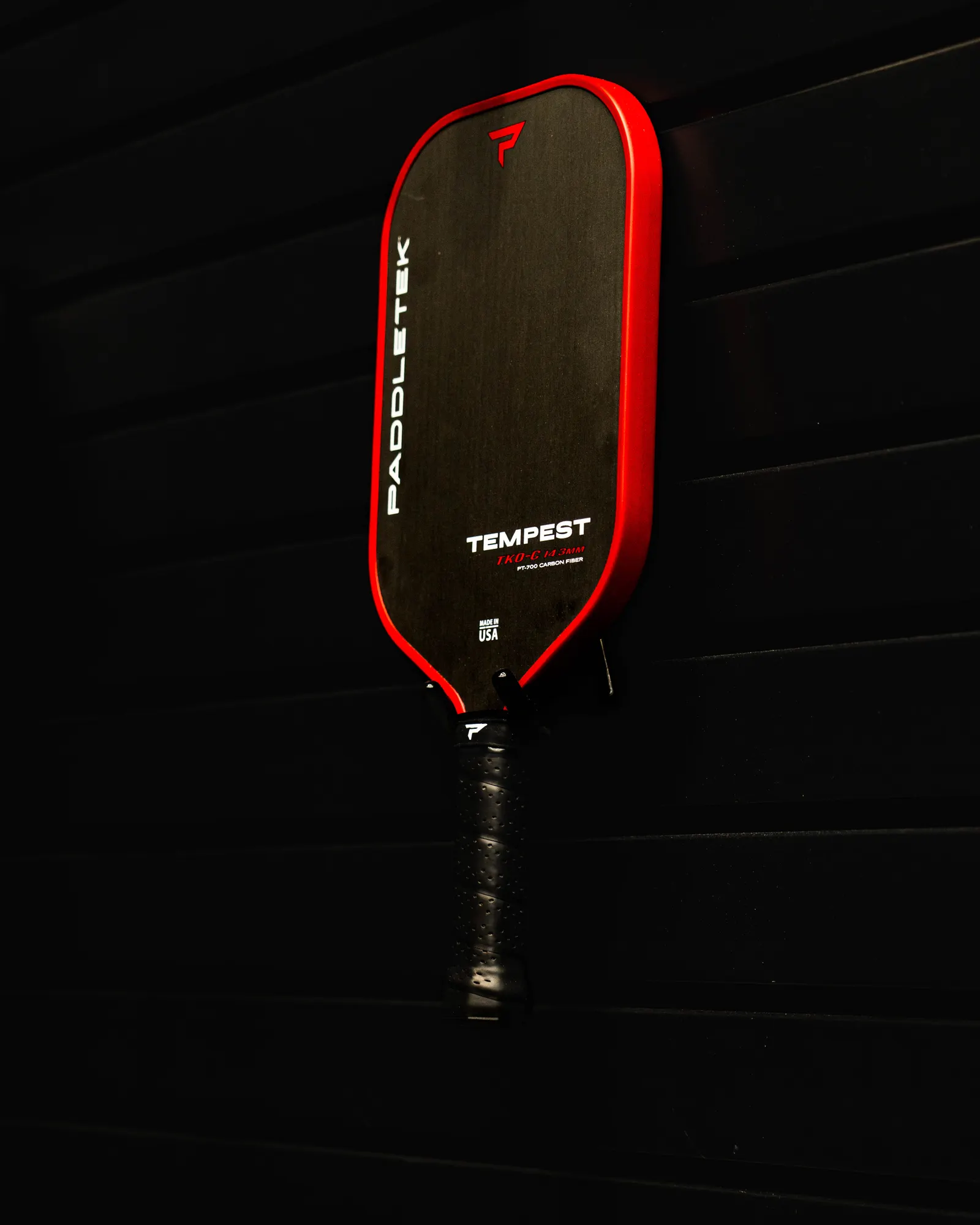 A red SUPR Pickleball paddle hung on a dark wall