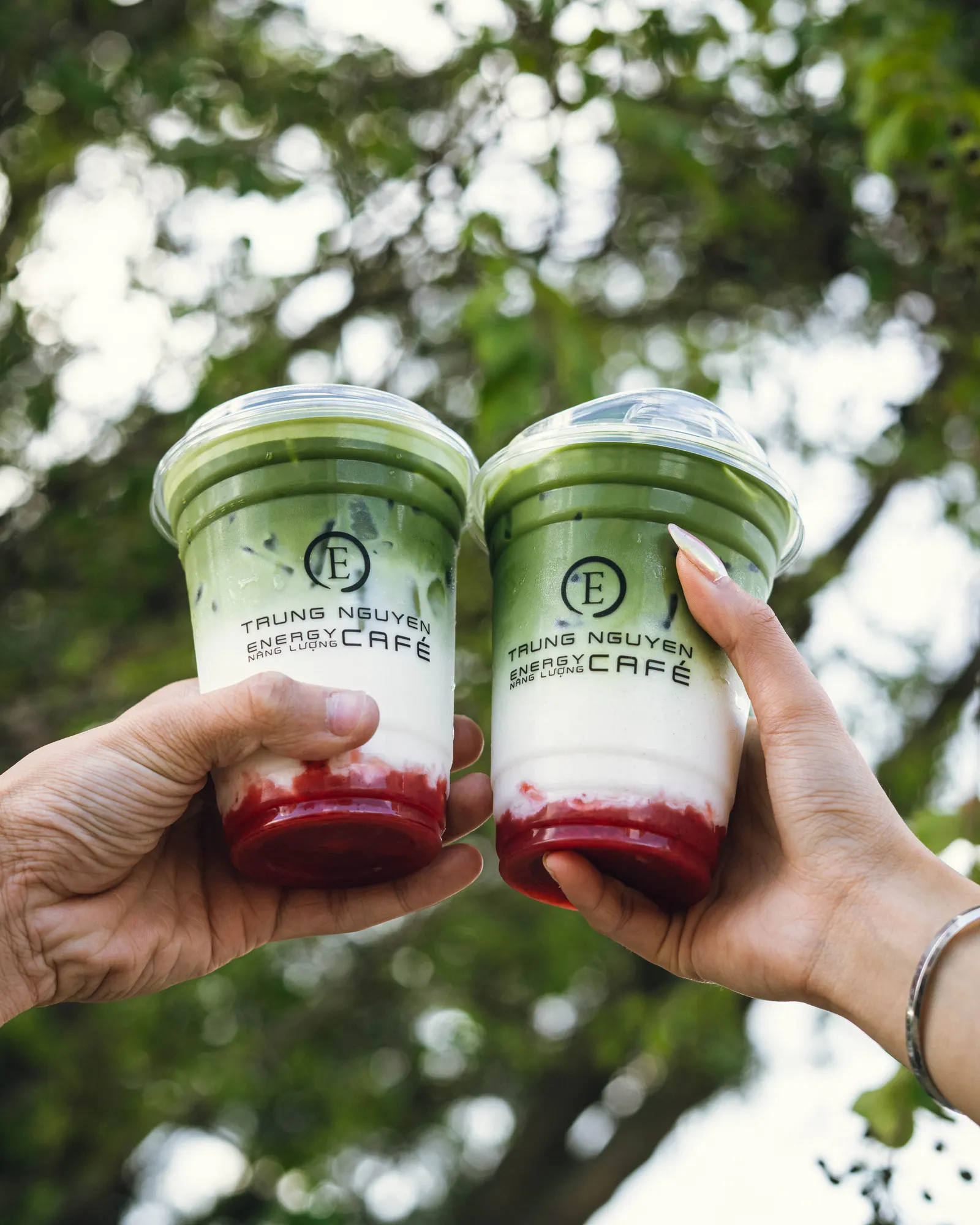 Two Trung Nguyen E Coffee drinks raised in a toast under the trees